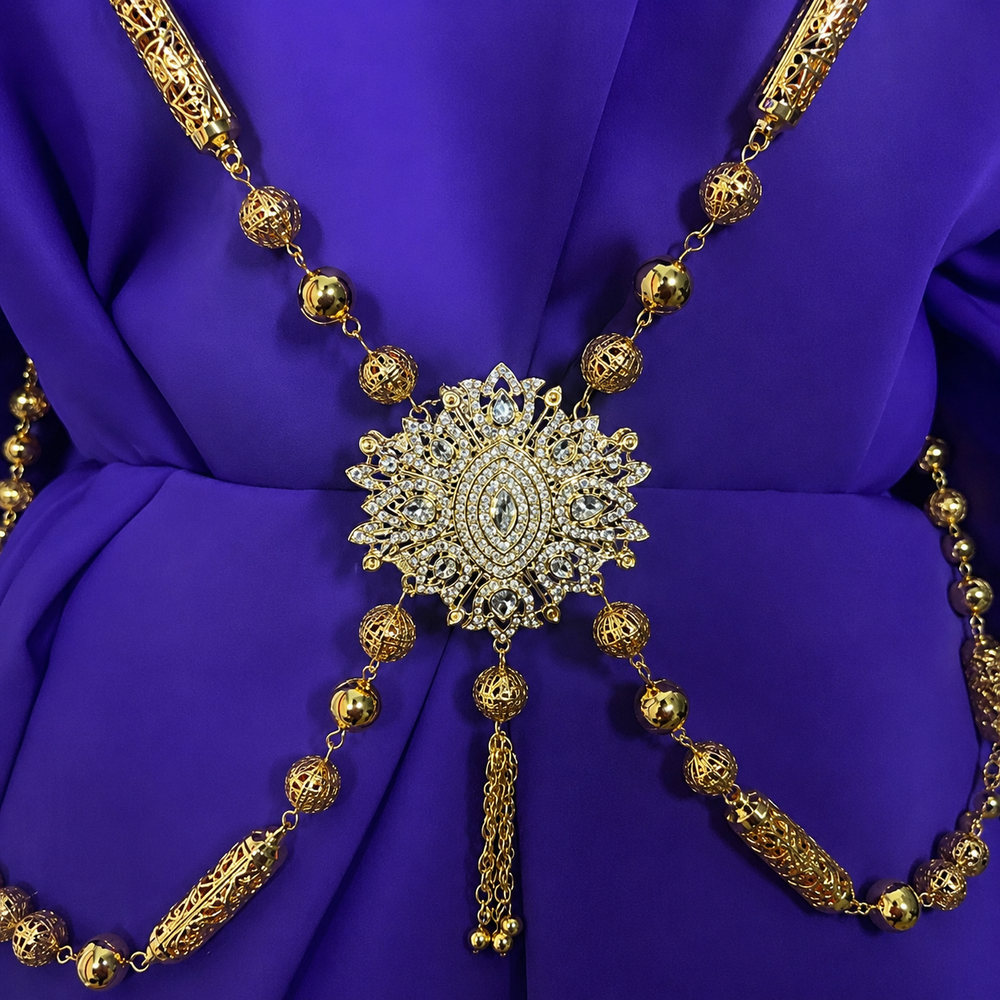 Traditional Moroccan Hamela gold chain featuring intricate filigree detailing, crystal centerpiece accents, and elegant draped chains styled on rich purple fabric for luxury Moroccan caftan and occasion wear.
