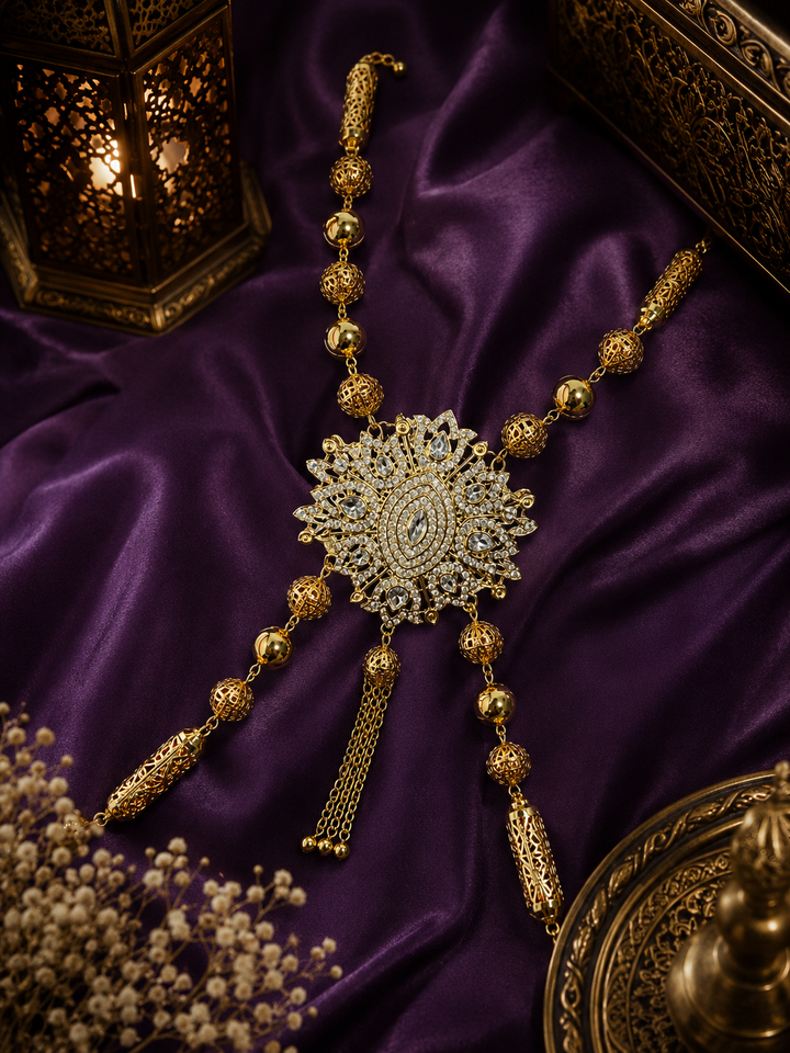 Traditional Moroccan Hamela gold chain featuring intricate filigree detailing, crystal centerpiece accents, and elegant draped chains styled on rich purple fabric for luxury Moroccan caftan and occasion wear.
