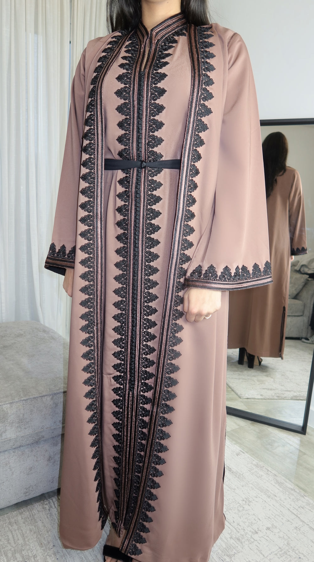 A woman wearing a traditional beige Moroccan caftan with black embroidery and a belt.
